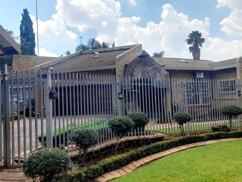 Front view of a brick-faced house featuring a combination of tiled and thatched roofing, secured by steel fencing and a well-maintained garden.