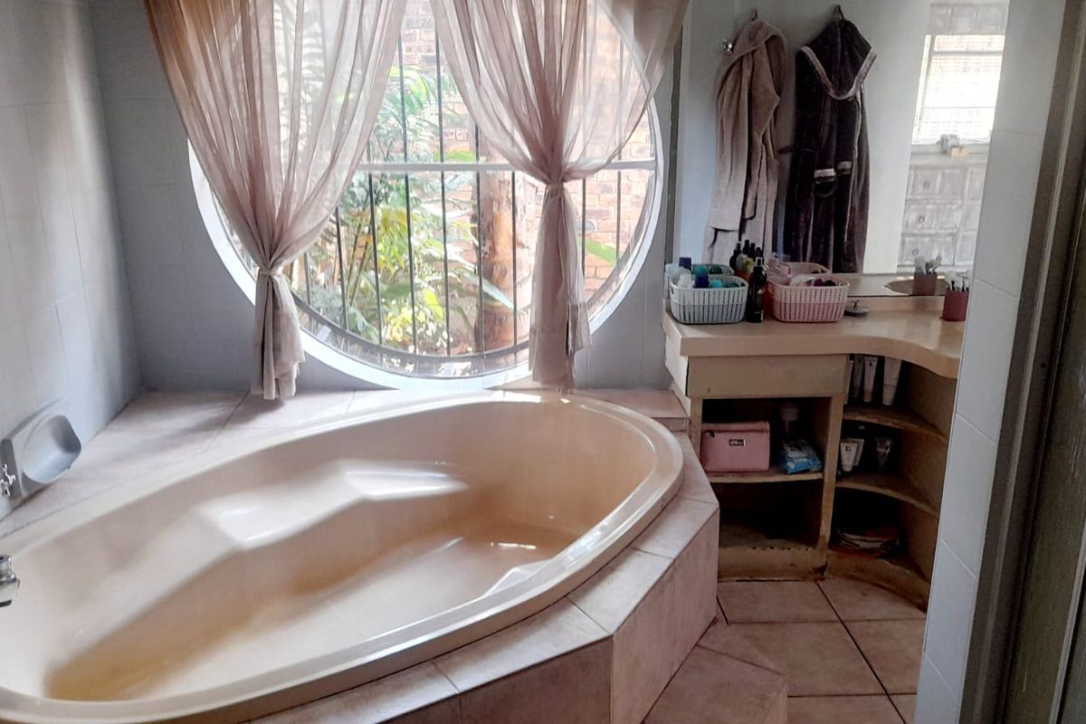 Bathroom featuring a built-in bathtub, tiled vanity, and a unique circular window with security bars, offering a functional space with potential for modernization.