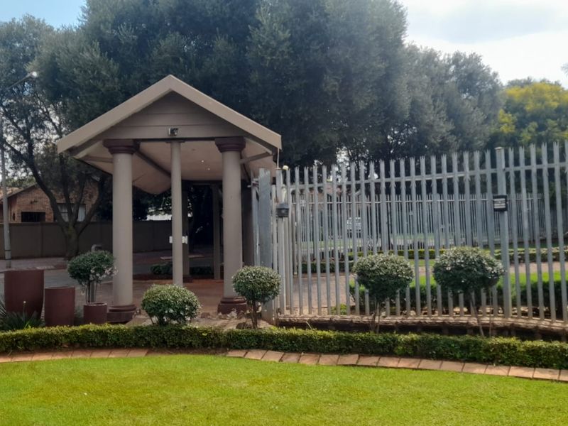 A well-maintained front entrance featuring a covered portico with columns, secure steel palisade fencing, and a neatly landscaped garden area.