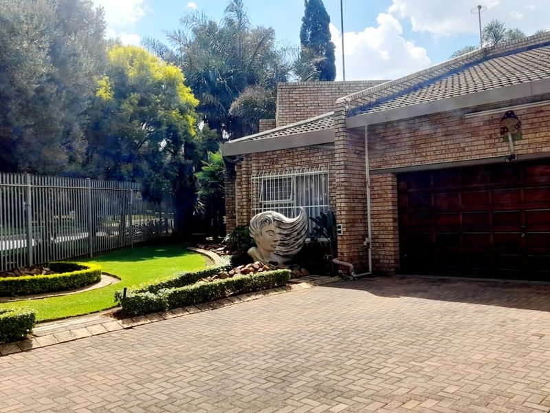 Front view of a brick-faced house featuring a paved driveway, sectional garage door, and well-maintained landscaped garden with security fencing.
