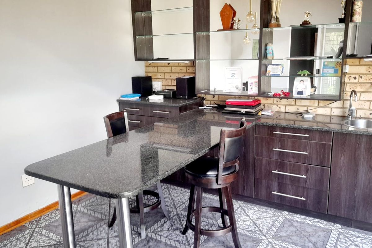 A kitchen area featuring dark wood cabinetry, granite countertops with an integrated breakfast bar, a stainless steel sink, and a brick feature wall.