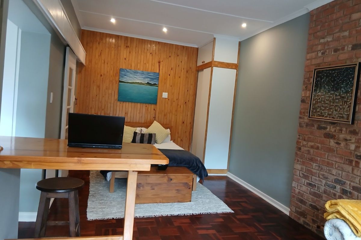 A bedroom featuring warm timber wall paneling, an exposed brick feature wall, and classic parquet flooring with integrated storage.