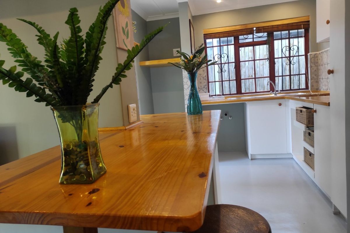 A functional kitchen featuring a wooden breakfast bar, built-in cabinetry, and a window with security bars, offering a clean and practical layout.