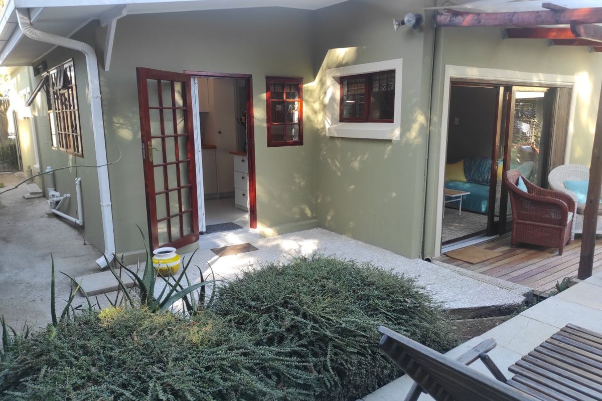 Rear exterior view of the apartment featuring a small patio area, timber-framed doors, and a wooden pergola structure.