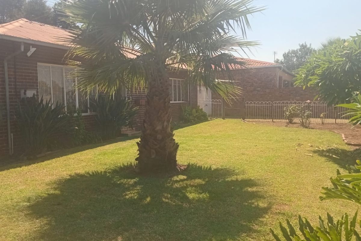A view of the rear garden featuring a brick exterior, tiled roof, and established landscaping with metal perimeter fencing.