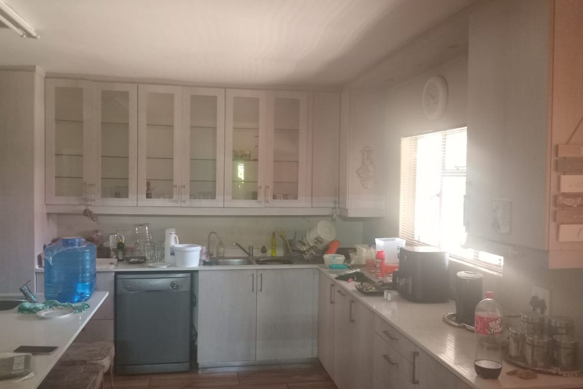 A functional kitchen featuring extensive built-in cabinetry, glass-fronted display cupboards, a stainless steel sink, and integrated dishwasher with ample countertop workspace.