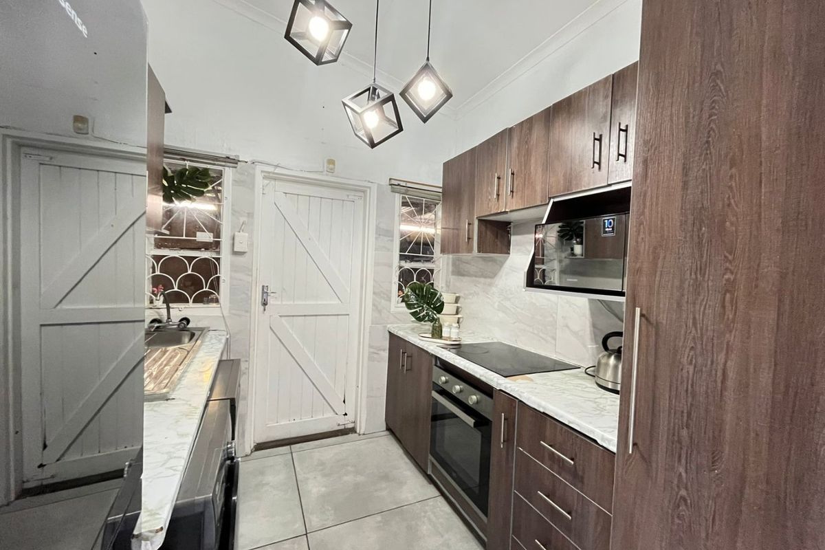 Modern galley-style kitchen featuring wood-grain cabinetry, marble-look countertops, integrated electric oven and hob, and contemporary pendant lighting.