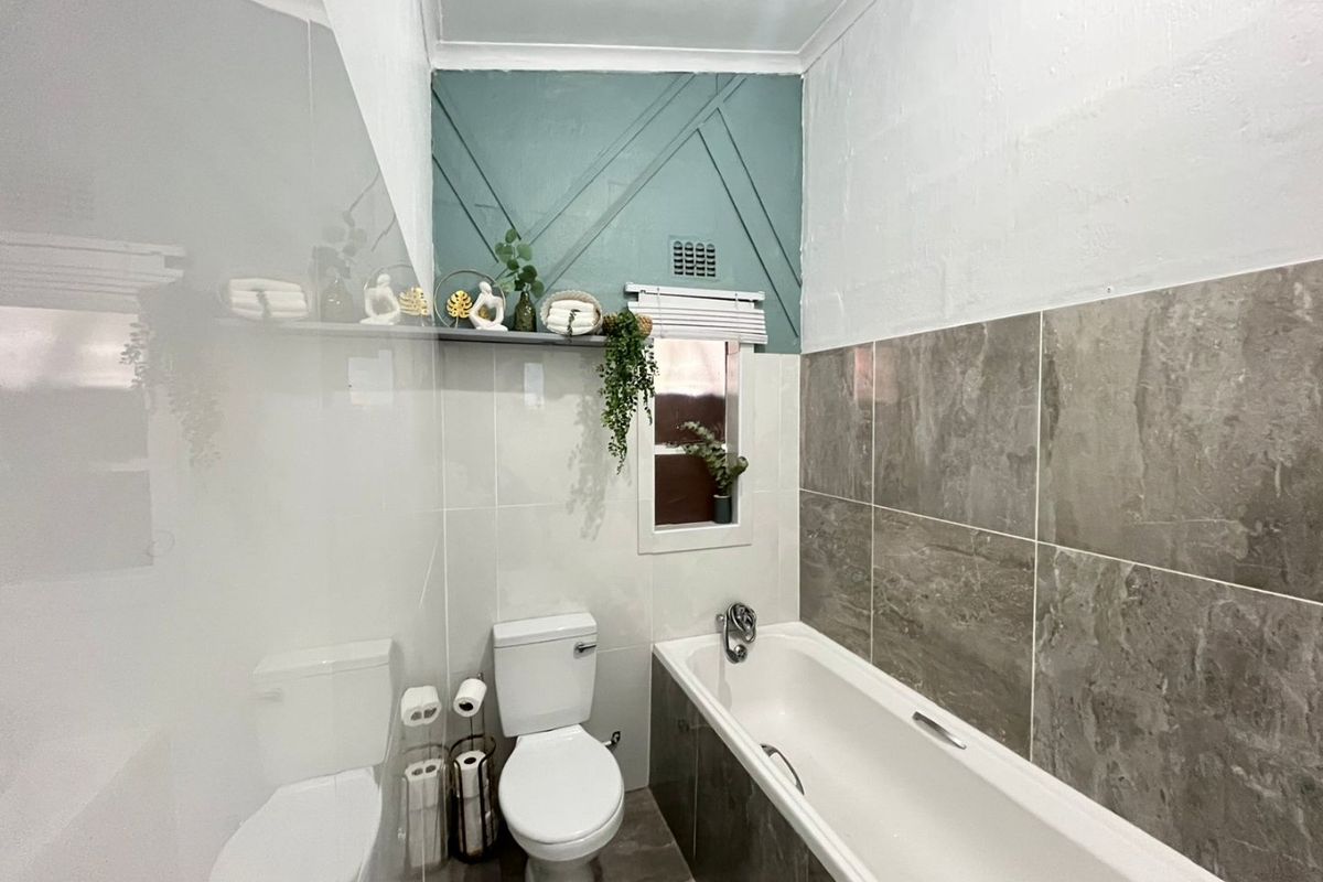 A modern bathroom featuring a bathtub, toilet, and stylish grey tiled walls with a decorative accent wall.