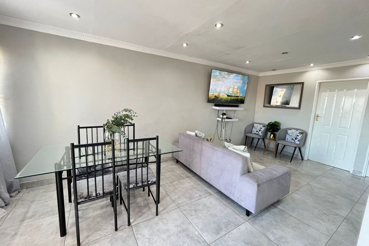 An open-plan living and dining area featuring neutral tiled flooring, recessed downlighting, and decorative ceiling cornicing.