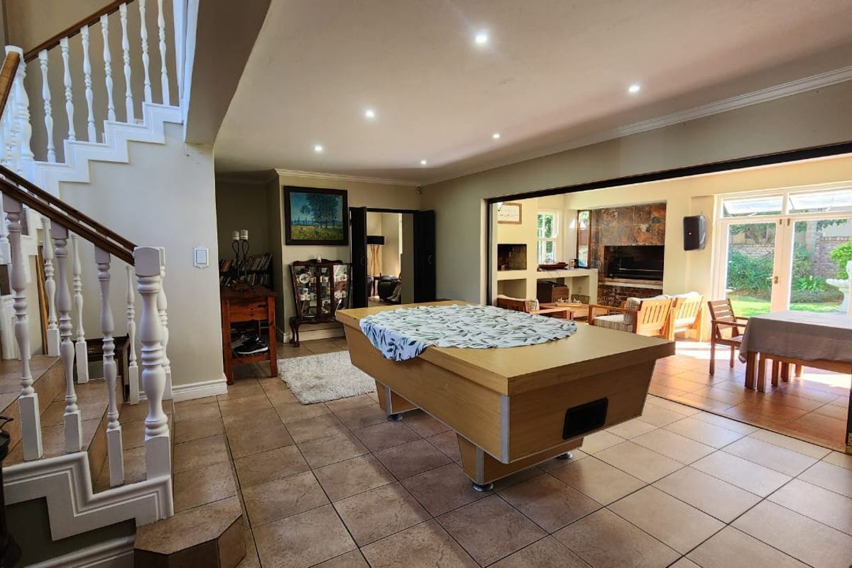 Spacious living area featuring tiled flooring, a staircase with white balustrades, and large bi-fold doors opening to an outdoor patio and fireplace area.