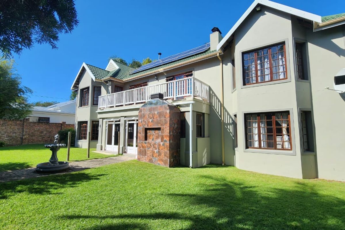 Rear view of a two-story house featuring a balcony, solar panels, and an outdoor fireplace set within a landscaped garden.