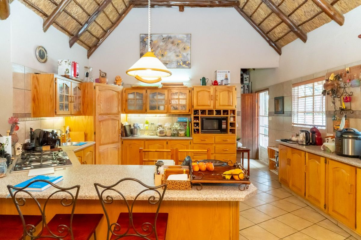 Spacious kitchen featuring timber cabinetry, granite countertops, a gas hob, and a high vaulted thatched ceiling with exposed timber beams.