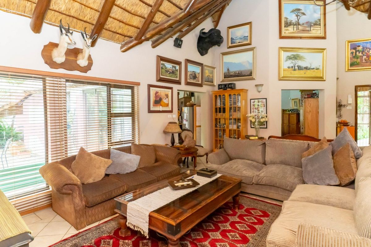 Spacious living room featuring a high vaulted thatched ceiling with exposed timber beams, tiled flooring, and large windows with fitted blinds.
