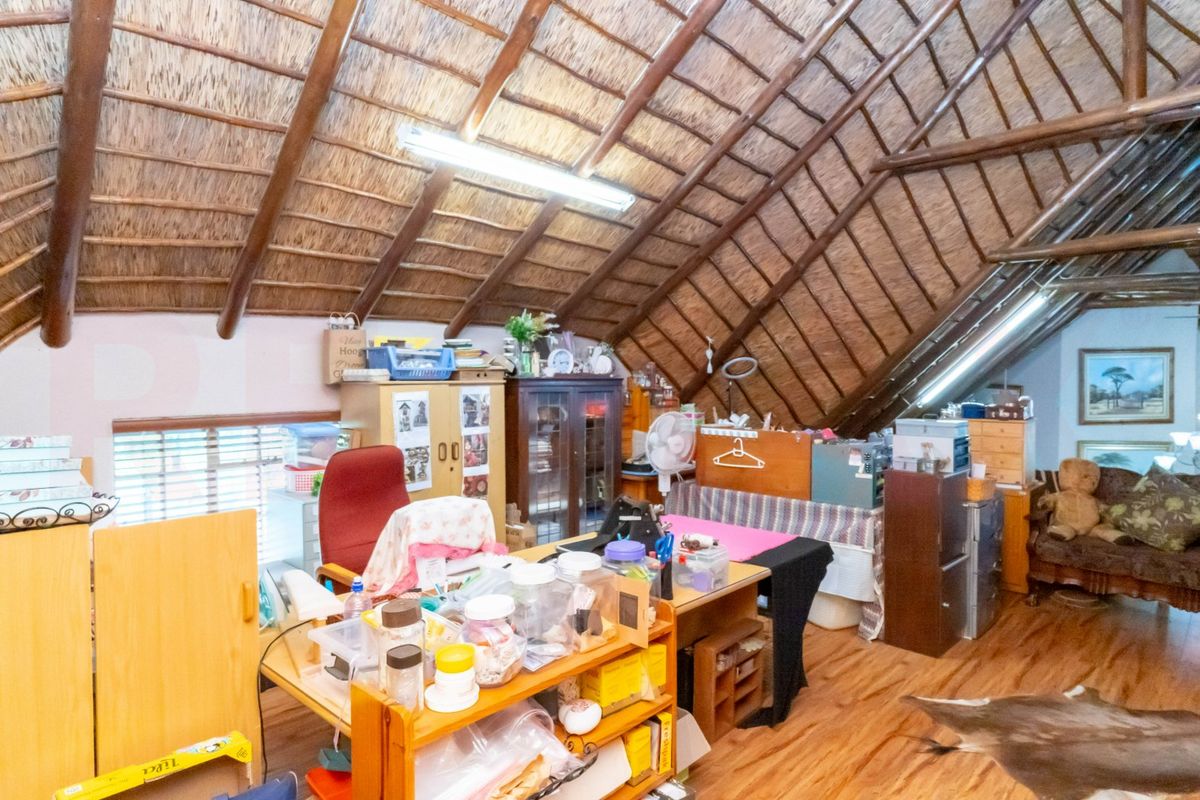 Attic-style bedroom or office space featuring a high vaulted thatched roof with exposed timber beams and laminate flooring.