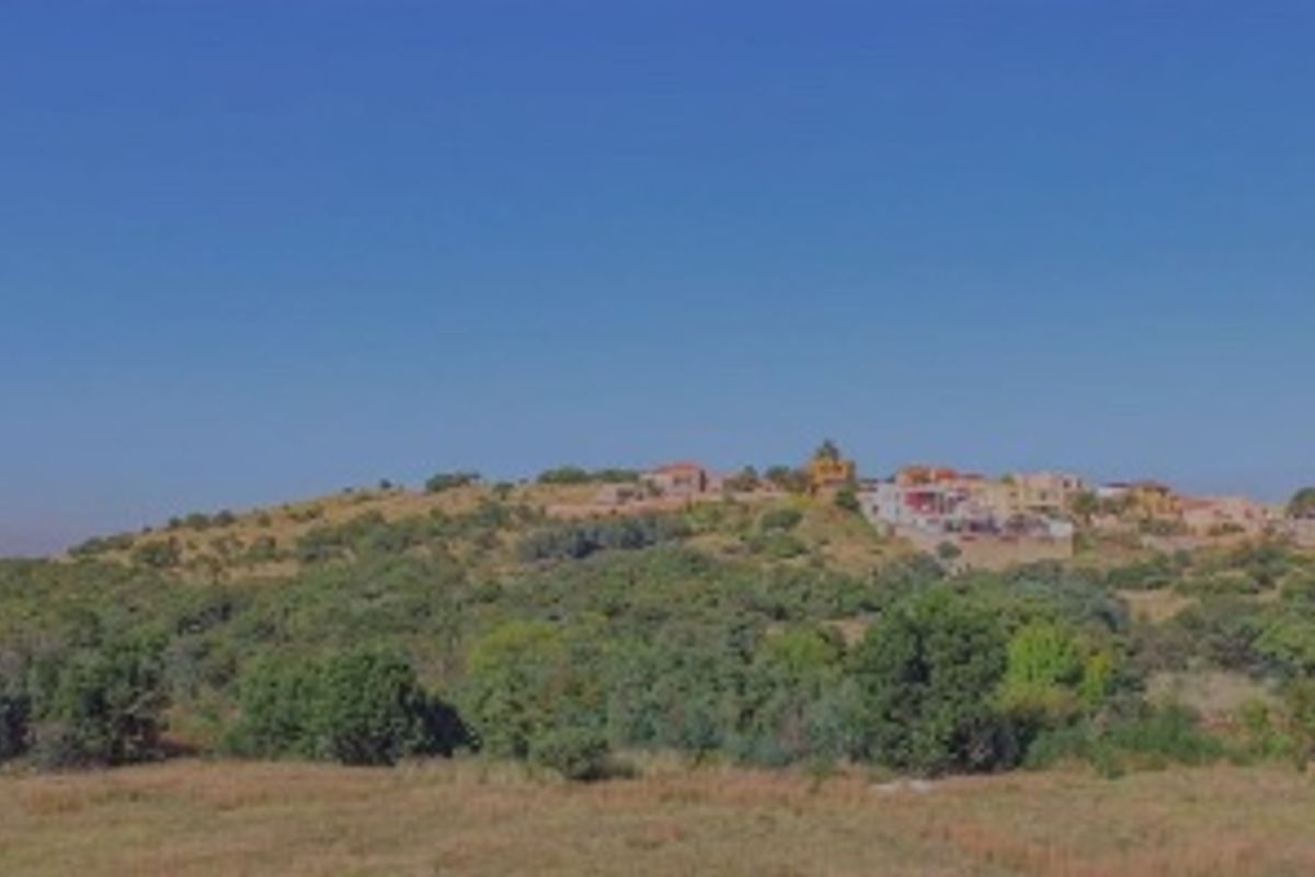A scenic landscape view of the surrounding terrain and distant residential buildings, showcasing the natural setting of the vacant land.