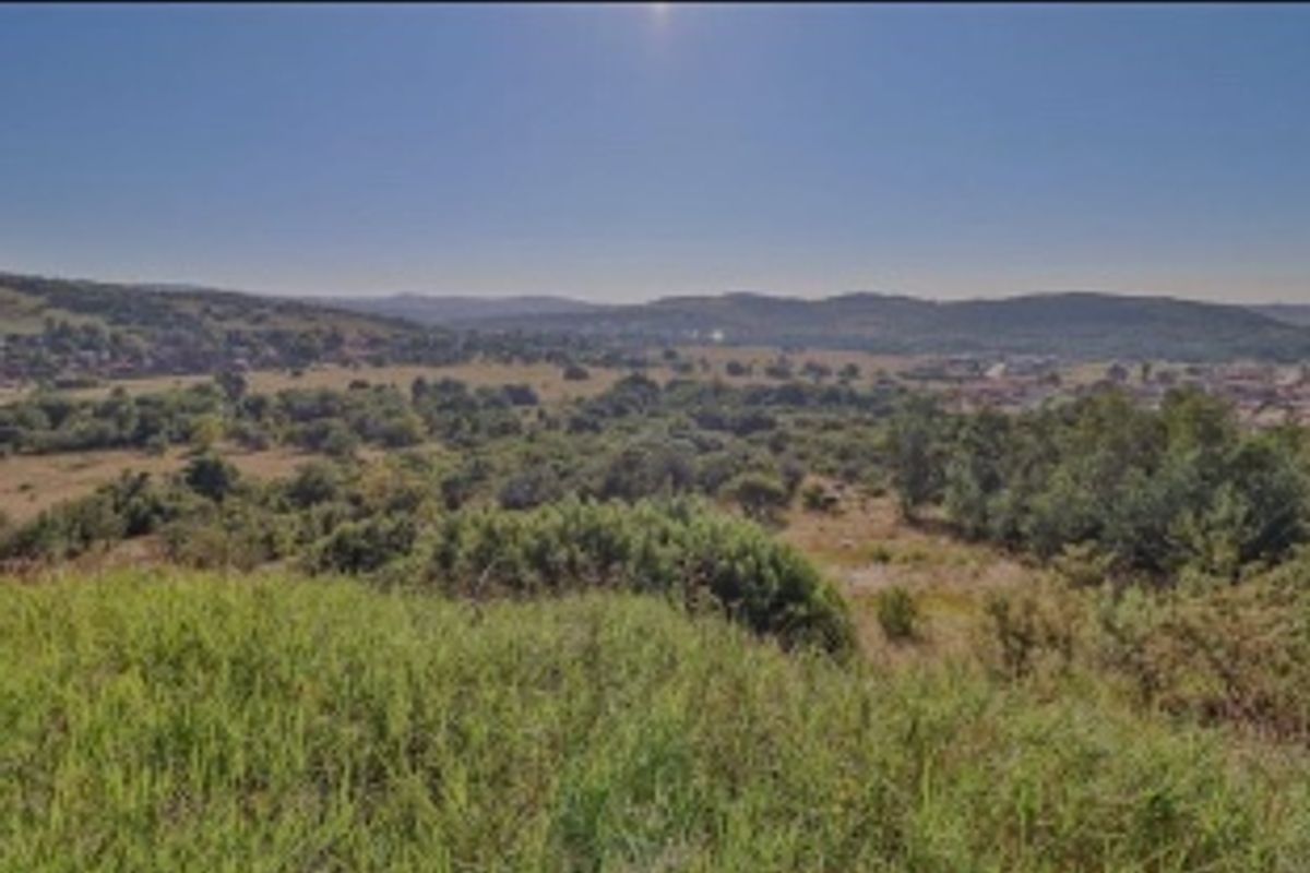 A wide-angle view of the vacant residential land, showcasing the natural landscape, surrounding vegetation, and distant hills.