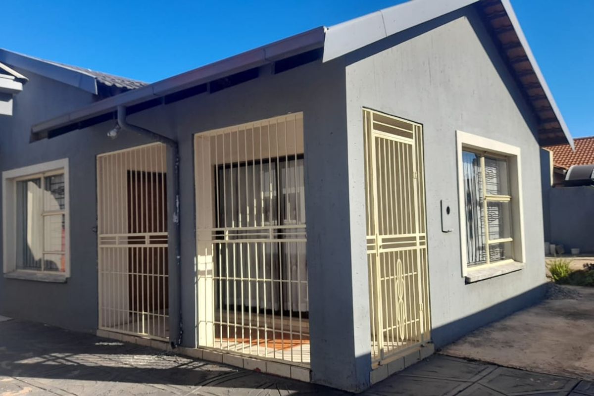 Rear exterior view of the house featuring grey painted walls, tiled roof, and fitted security gates over the sliding doors and windows.