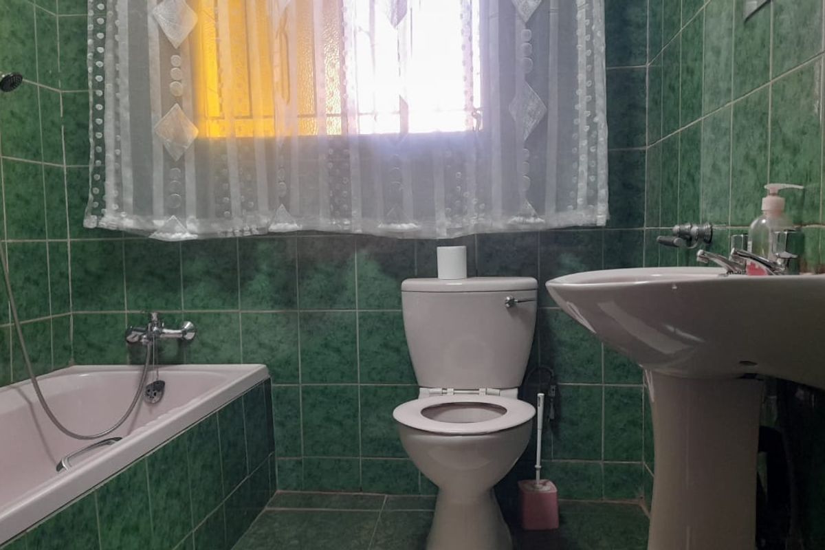 A dated bathroom featuring green tiled walls and flooring, equipped with a standard bathtub, pedestal basin, and toilet.