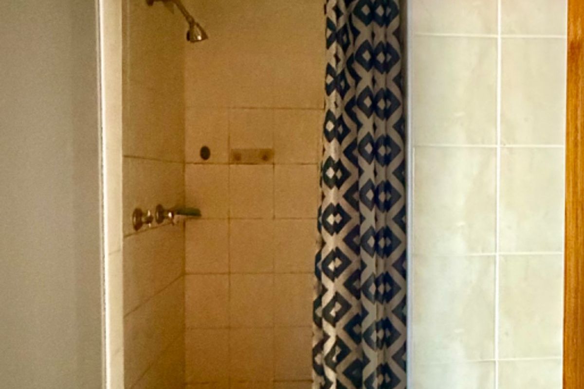 A dated shower enclosure featuring tiled walls and standard plumbing fixtures, requiring cosmetic updates to improve its overall appearance and functionality.