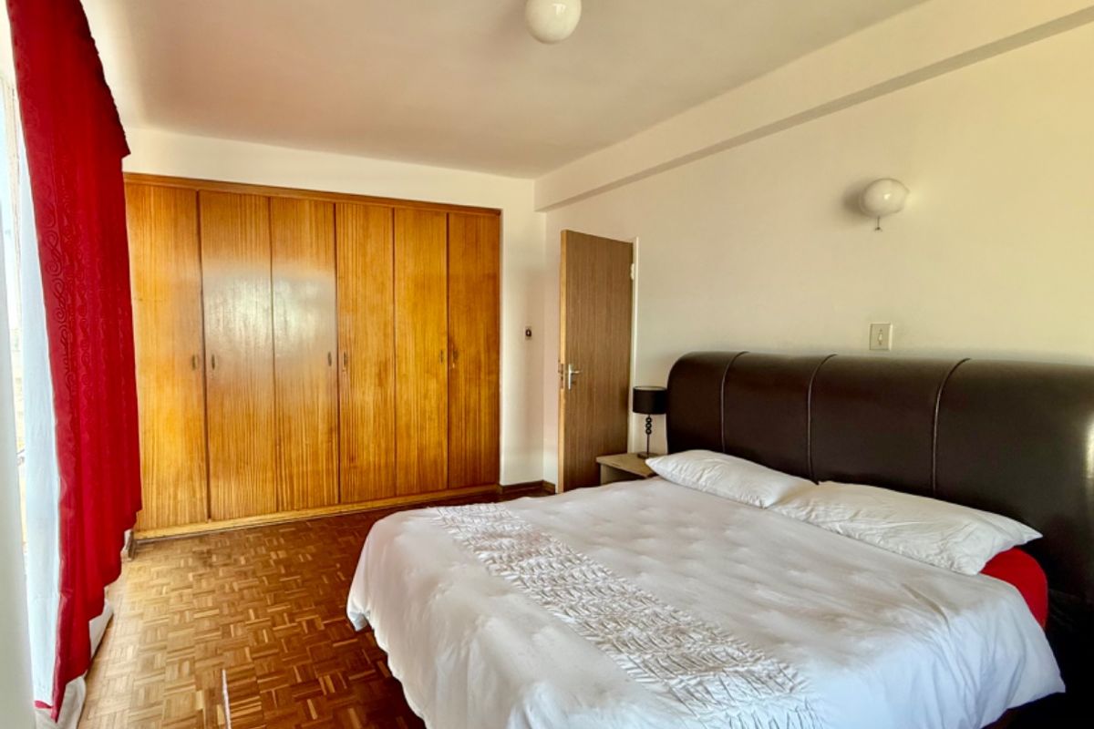 A spacious bedroom featuring classic parquet flooring and extensive built-in wooden cabinetry for storage.