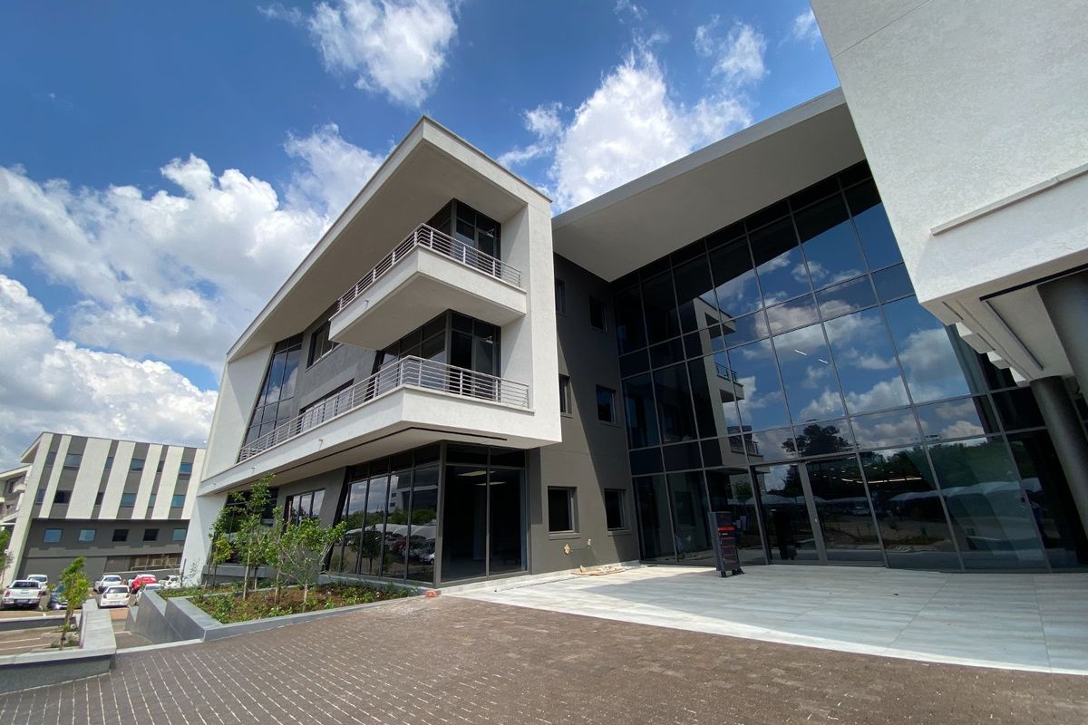 Modern commercial office building featuring a striking glass facade, multi-level balconies, and professional paved exterior grounds.