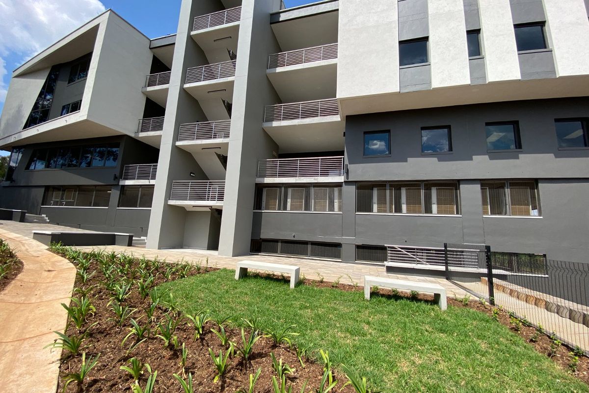 Modern multi-story commercial building exterior featuring clean architectural lines, private balconies, a central stairwell, and a well-maintained landscaped garden area.