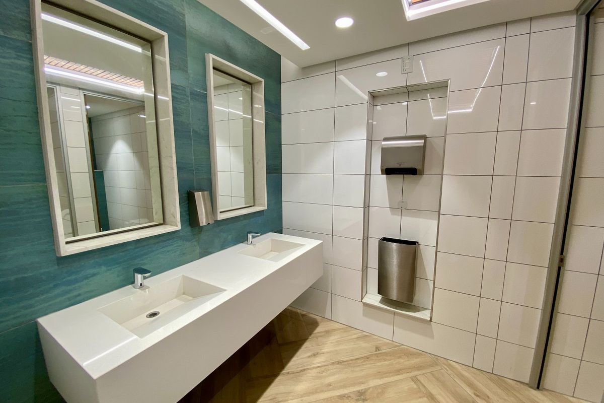 Modern commercial bathroom featuring a sleek double vanity, recessed mirrors, contemporary wall tiling, and integrated wall-mounted fixtures for a clean, professional aesthetic.