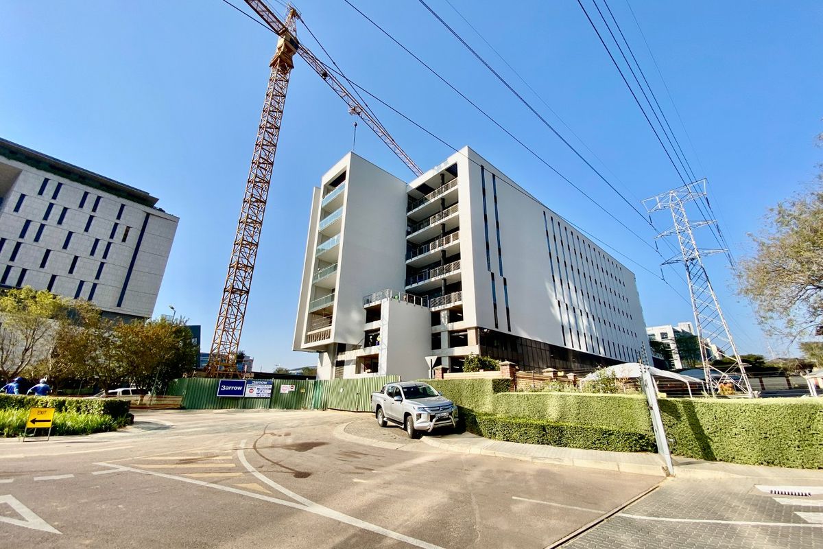 Exterior view of a modern commercial building currently under construction, featuring multiple balconies and a large construction crane on site.