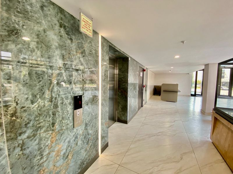 Modern commercial building lobby featuring high-end marble wall cladding, polished porcelain flooring, and integrated elevator access with contemporary recessed lighting.