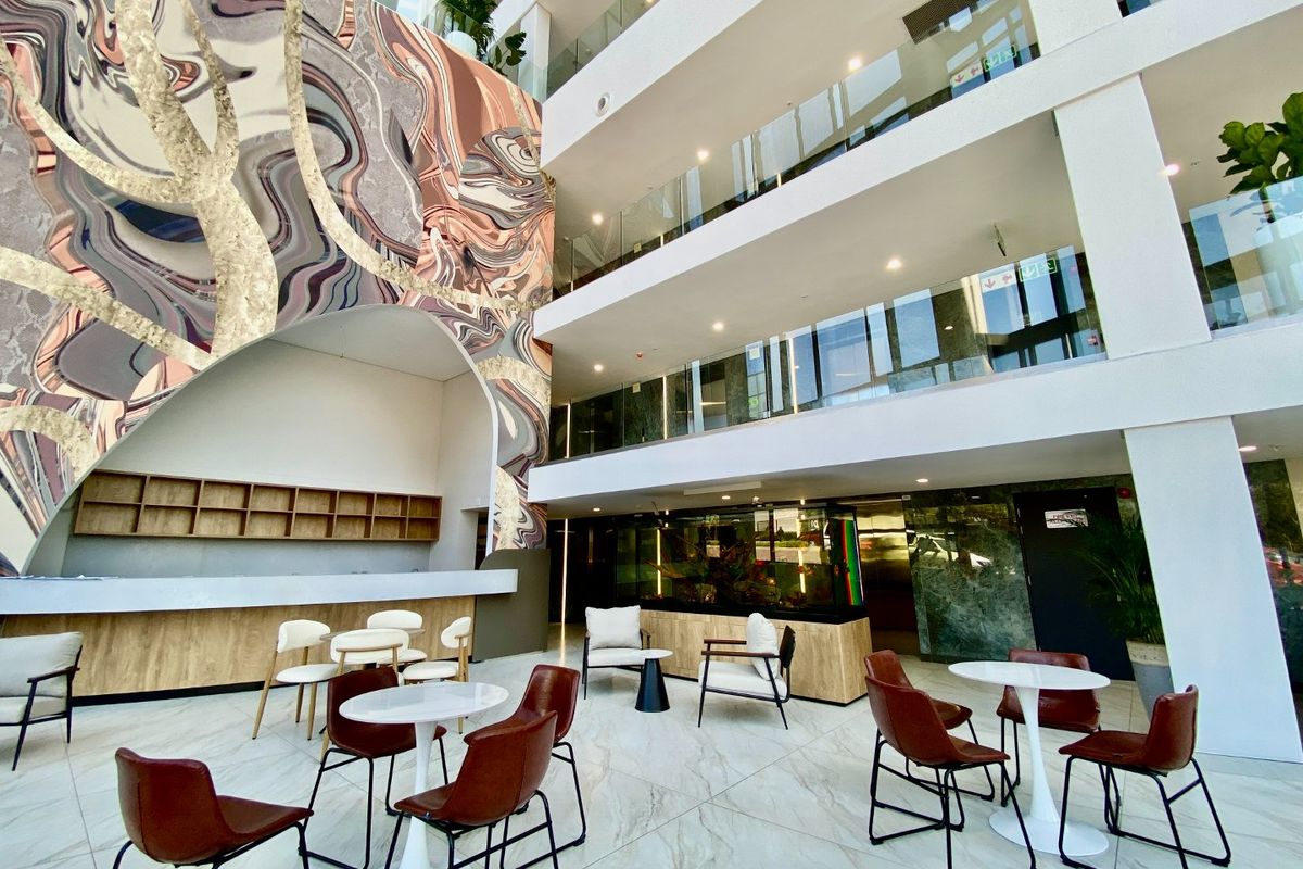 Modern multi-level commercial atrium featuring high ceilings, glass balustrades, marble-look flooring, and a decorative feature wall with a built-in service counter.
