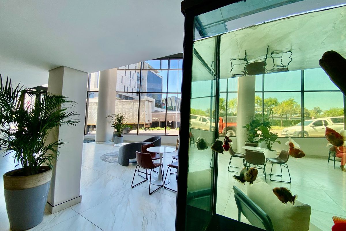 Modern commercial lobby entrance featuring expansive floor-to-ceiling windows, polished marble-look tile flooring, and structural columns, creating a bright and professional reception area.