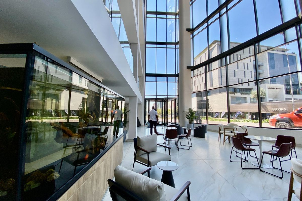 Spacious commercial lobby featuring floor-to-ceiling glass walls, high ceilings, and polished marble-look flooring, creating a bright and professional entrance area.