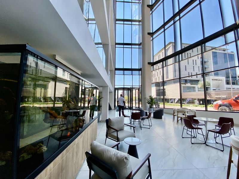 Spacious commercial lobby featuring floor-to-ceiling glass walls, high ceilings, and polished marble-look flooring, creating a bright and professional entrance area.