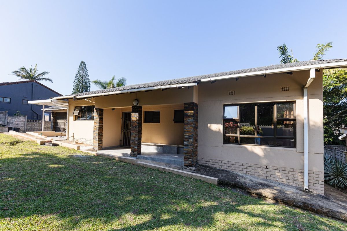 Rear view of the house featuring a covered patio with stone-clad pillars, aluminium windows, and a large surrounding garden area.