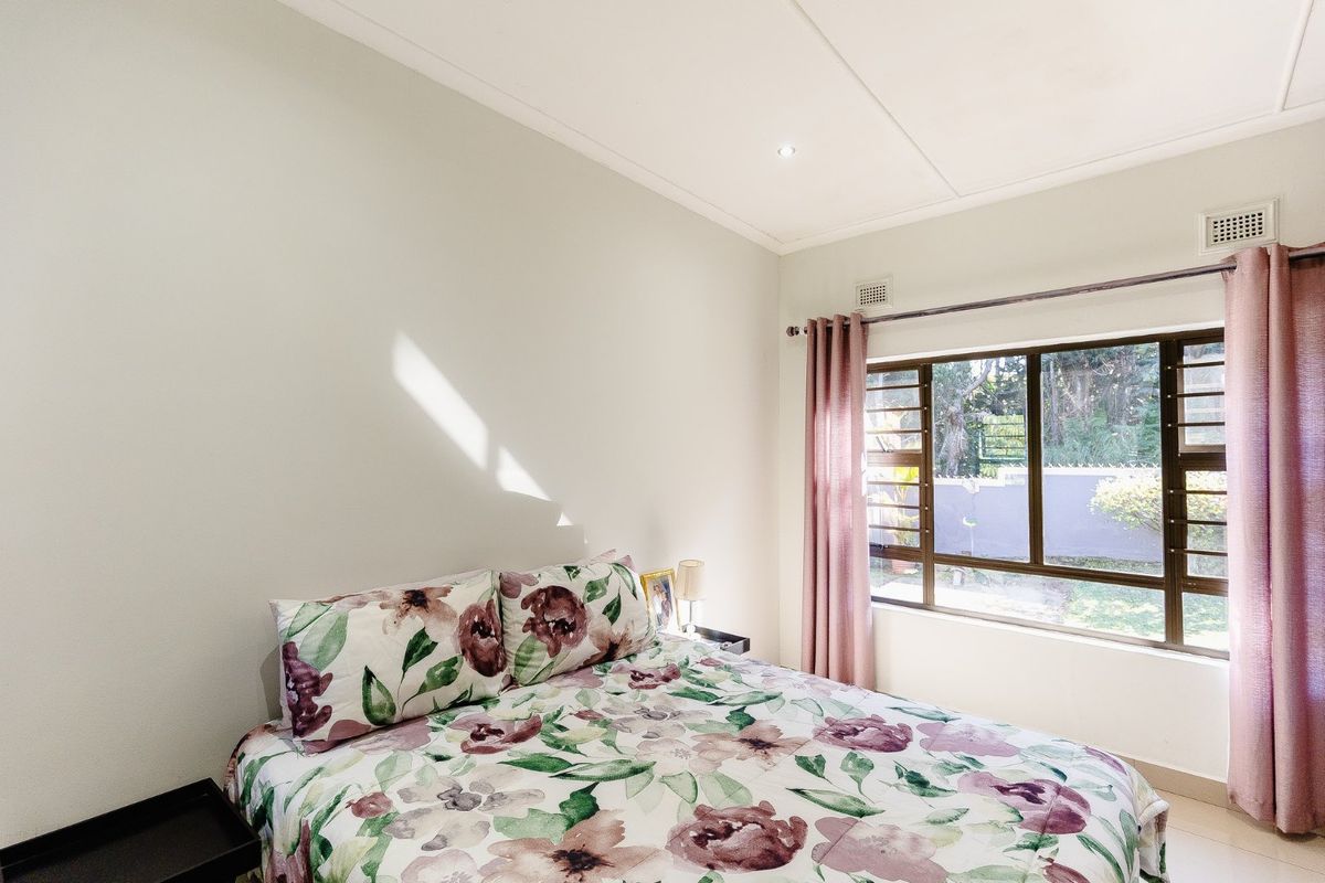 A bright bedroom featuring a large aluminium-framed window with garden views, neutral walls, and recessed ceiling lighting.