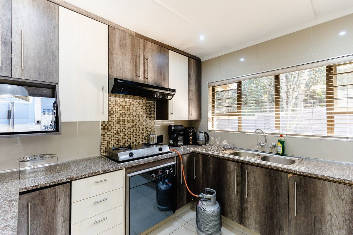 Modern kitchen featuring two-tone cabinetry, granite countertops, a gas hob with extractor fan, and a double basin sink with tiled backsplash.