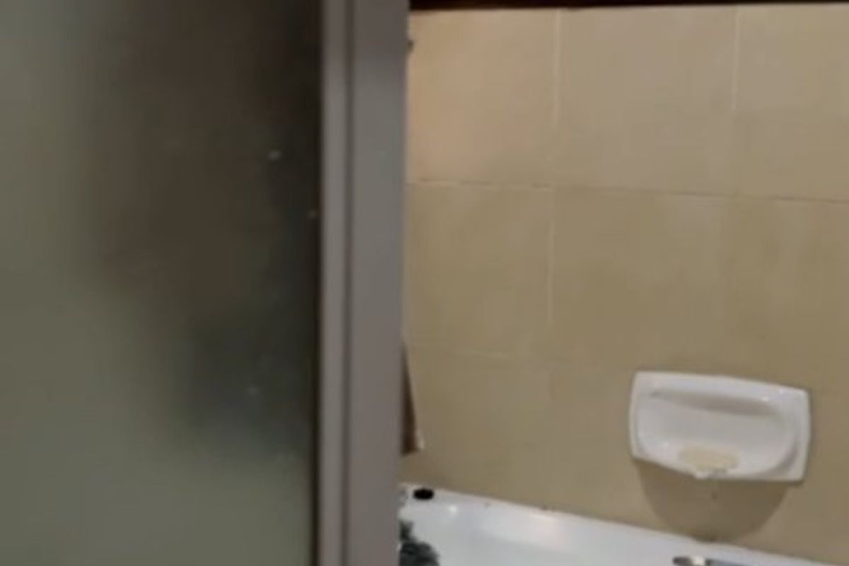 A functional bathroom featuring a standard bathtub, toilet, and tiled wall finishes, viewed through a frosted glass door.