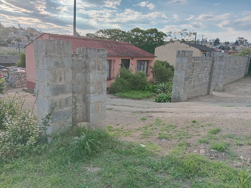 Front view of a single-story house featuring a tiled roof, security bars on windows, and an unfinished concrete block boundary wall.