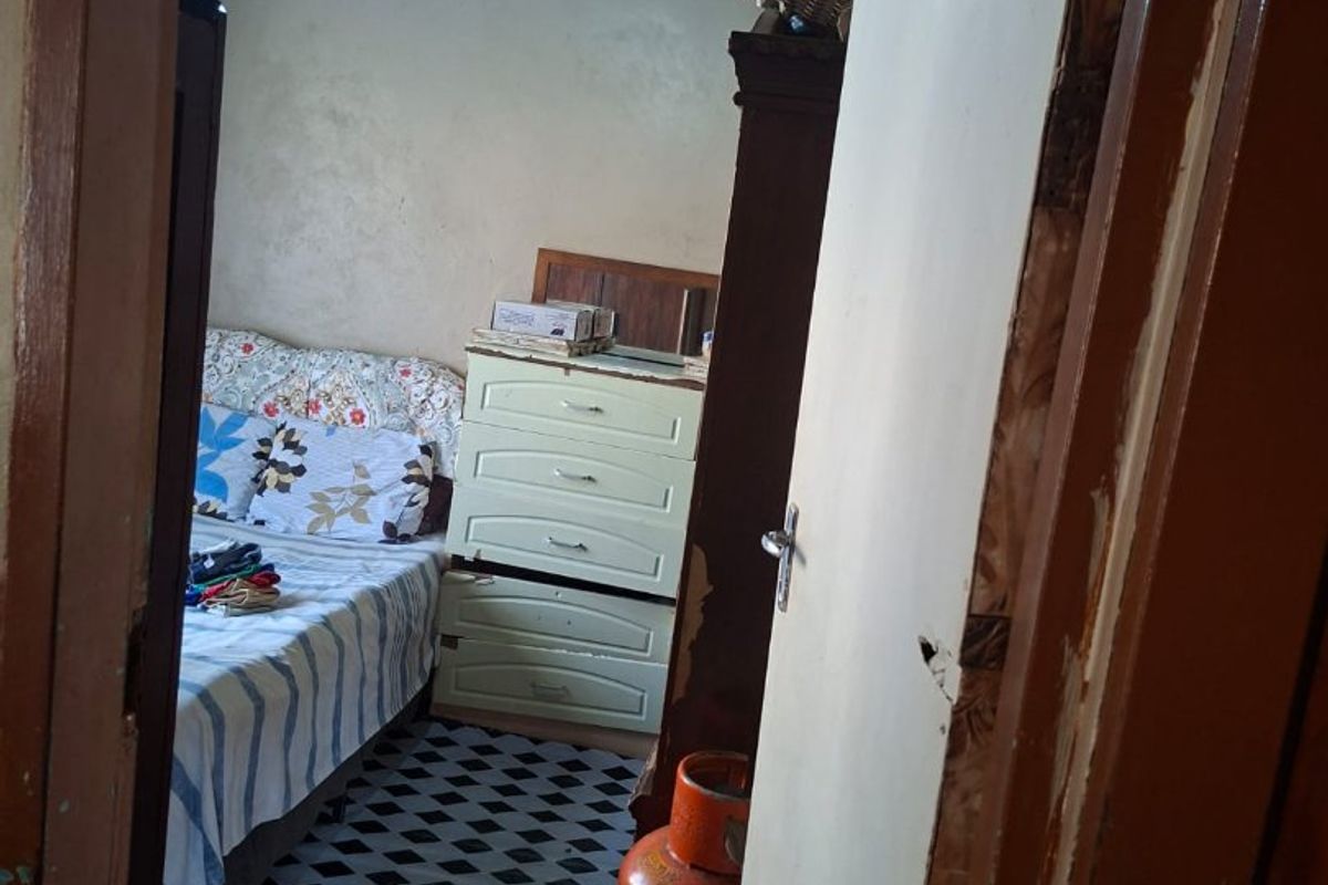 A bedroom featuring exposed rafters and tiled flooring, currently showing significant signs of wear and requiring maintenance to the door frame and wall finishes.