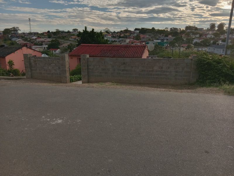 A street-level view showing an asphalt road and an unfinished concrete block boundary wall surrounding the property.