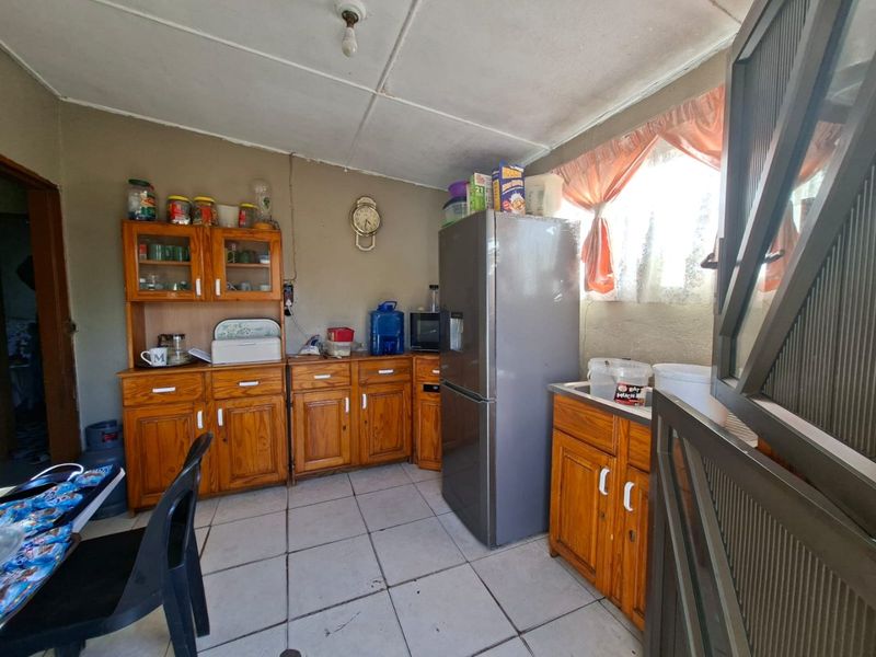A functional kitchen featuring wooden cabinetry, tiled flooring, and a window, offering a dated aesthetic with potential for modernization.