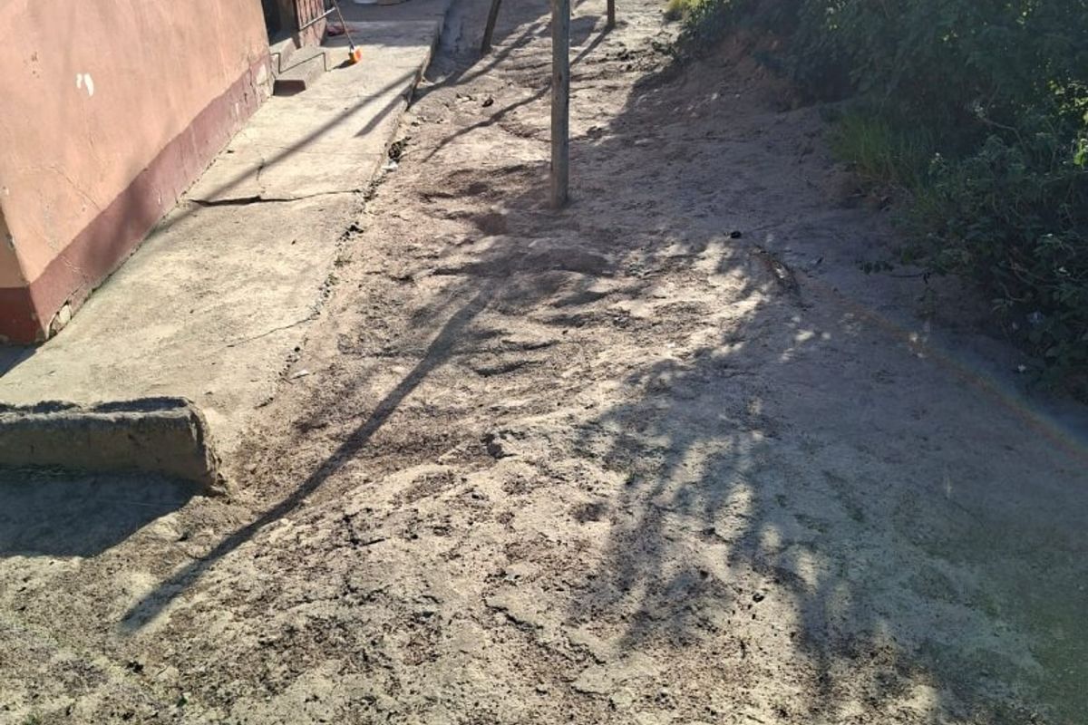 Rear exterior area featuring a concrete pathway, unlandscaped ground, and access to the property via a security gate.
