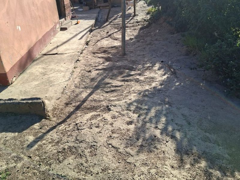 Rear exterior area featuring a concrete pathway, unlandscaped ground, and access to the property via a security gate.