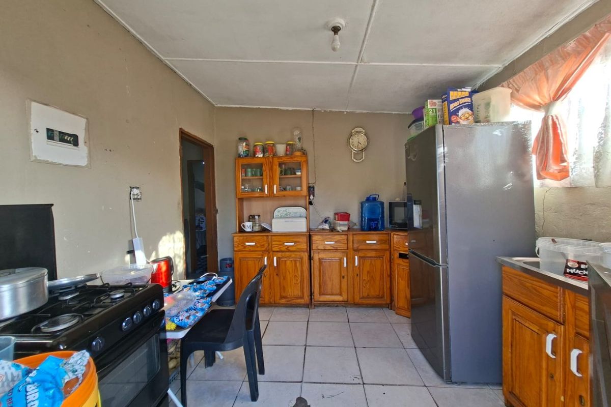 A functional kitchen featuring wooden cabinetry, tiled flooring, and a gas stove, requiring cosmetic updates to improve its overall condition and aesthetic appeal.