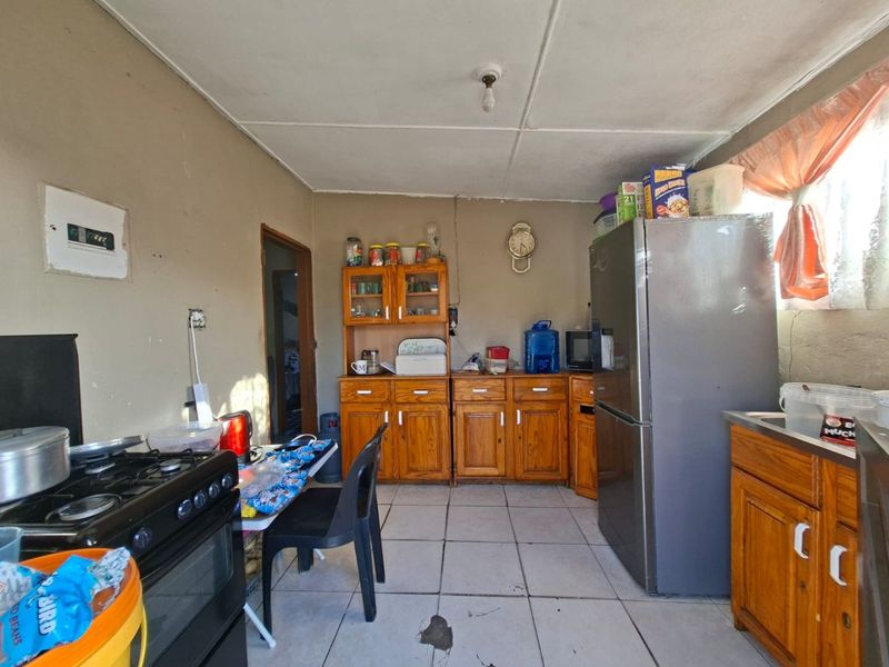 A functional kitchen featuring wooden cabinetry, tiled flooring, and a gas stove, requiring cosmetic updates to improve its overall condition and aesthetic appeal.