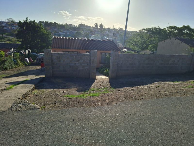 Front view of a residential property featuring a tiled roof house enclosed by a concrete block boundary wall and a paved driveway area.