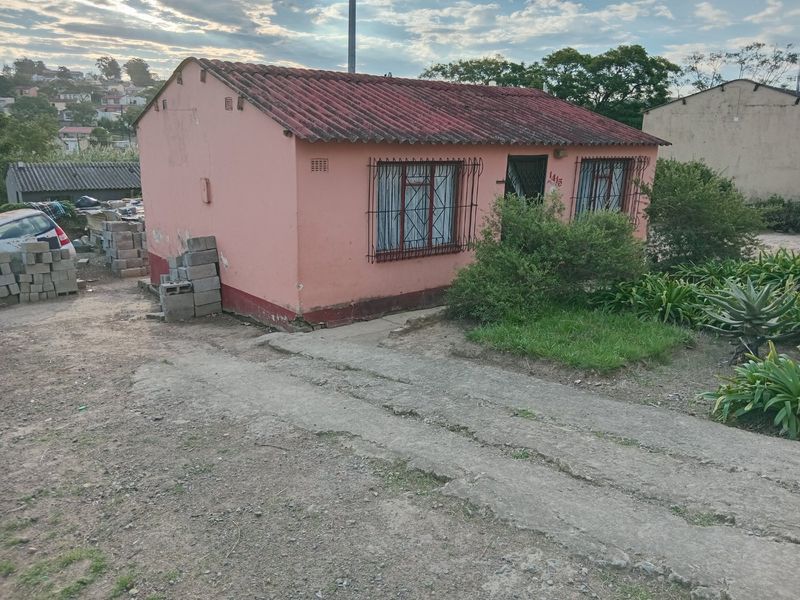 Front view of a single-story detached house featuring a concrete driveway, security bars on windows, and a tiled roof in need of maintenance.
