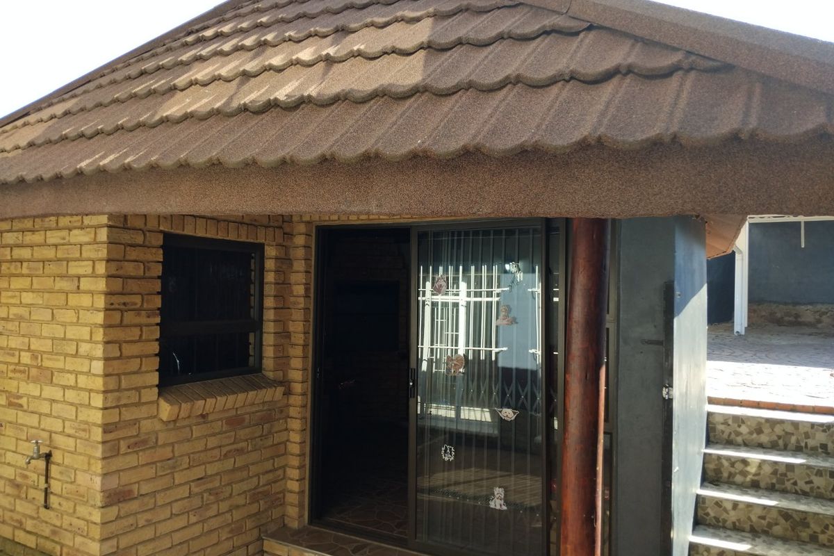 Rear exterior view of a facebrick structure featuring a tiled roof, sliding glass door with security gate, and external staircase.