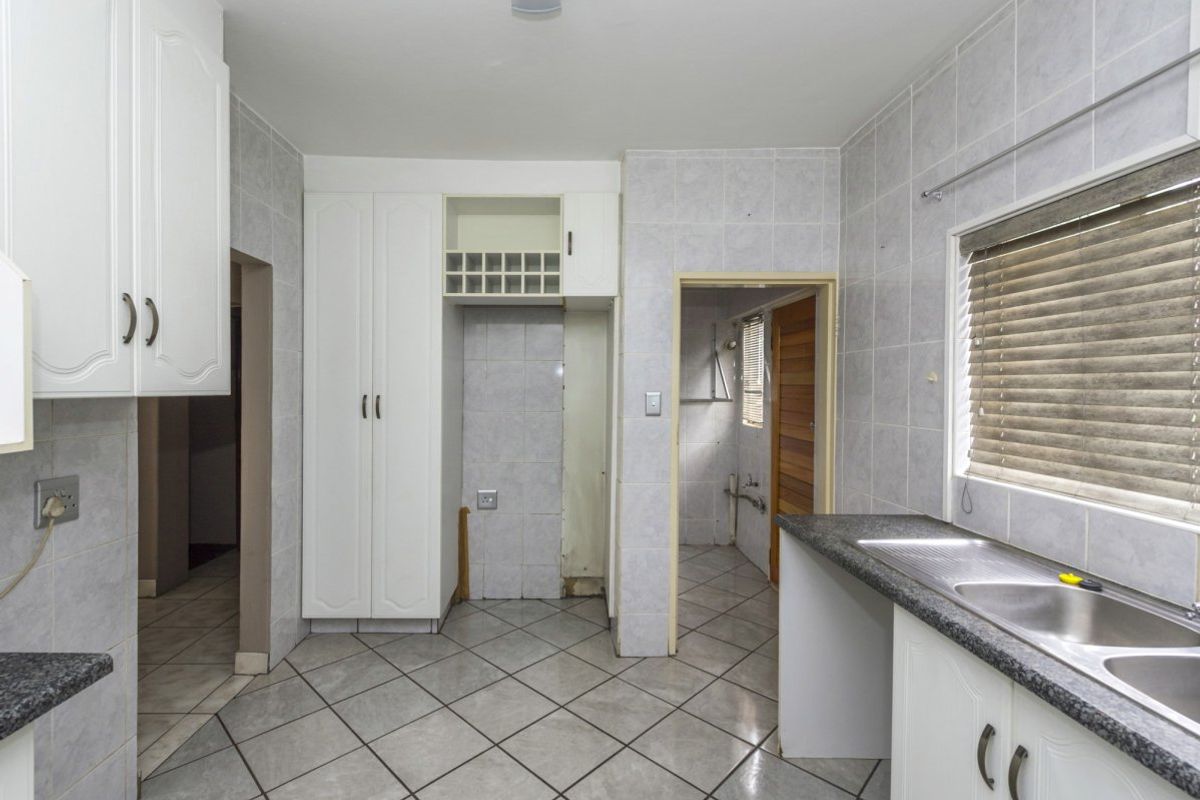 A dated kitchen featuring tiled walls and floors, granite countertops, and built-in cabinetry with an integrated wine rack, requiring cosmetic updates.