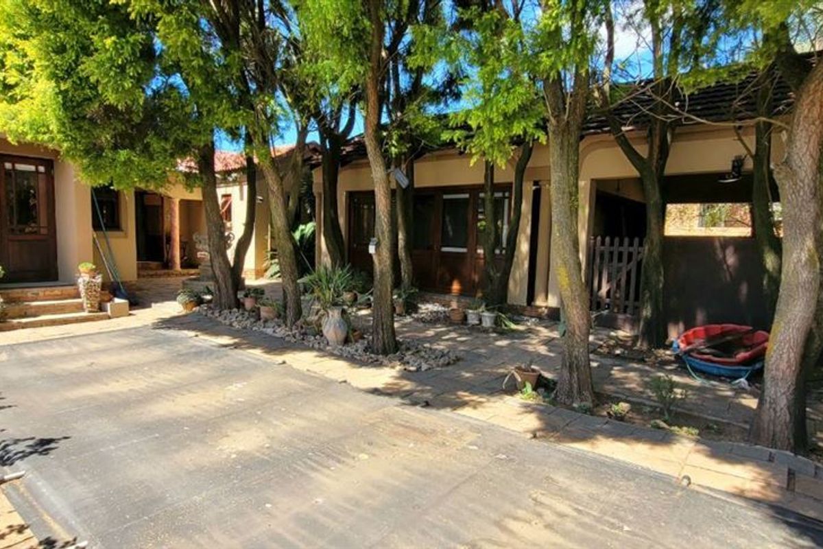 A shaded outdoor pool area featuring a paved patio, mature trees, and direct access to the main residence through timber-framed doors.